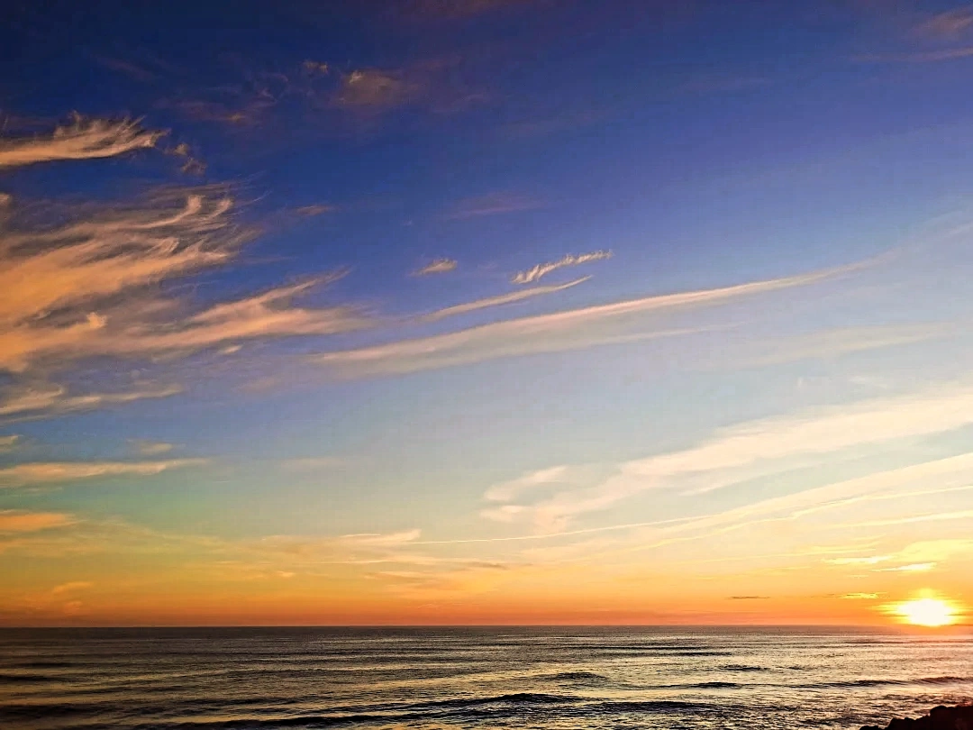 Wispy pink and orange clouds over the ocean at sunset